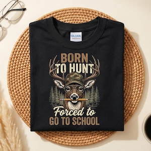 May include: Black t-shirt featuring a deer graphic wearing a camouflage hat and glasses, holding a pencil. The text reads "BORN TO HUNT" above the deer and "FORCED TO GO TO SCHOOL" below.