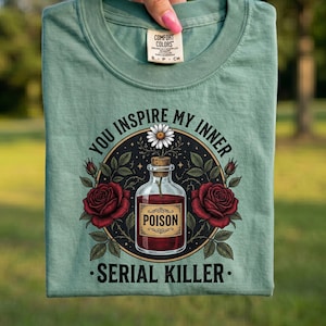 May include: Light green t-shirt with a graphic design. The design features a bottle labeled "POISON" surrounded by roses and the text "YOU INSPIRE MY INNER SERIAL KILLER."