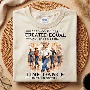 Könnte beinhalten: Ein cremefarbenes T-Shirt mit einer Grafik von fünf Personen in Cowboyhüten und Westernkleidung, die einen Line Dance tanzen. Der Text lautet: ALL WOMEN ARE CREATED EQUAL ONLY THE BEST STILL LINE DANCE IN THEIR SIXTIES. Das Shirt hat einen Rundhalsausschnitt.