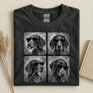 May include: A charcoal gray crew neck t-shirt featuring a graphic print of four black and white portraits of a dog wearing sunglasses. The Gildan brand tag is visible at the inner neckline, showing the size S and the country of origin.