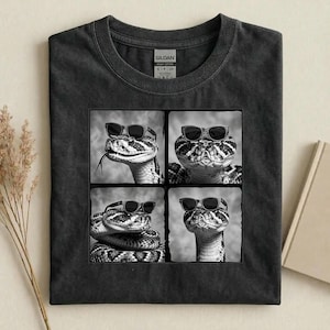 May include: Dark grey t-shirt with a four-panel image of a snake wearing sunglasses. The snake is black and white with a patterned design. One panel shows the snake with its tongue out. The shirt has a crew neck and short sleeves.