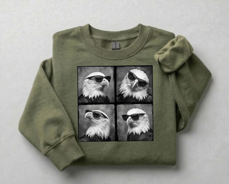 May include: An olive green sweatshirt featuring a black and white graphic of four eagles wearing sunglasses. The eagles are in a square grid pattern. The sweatshirt has a crew neck and long sleeves.