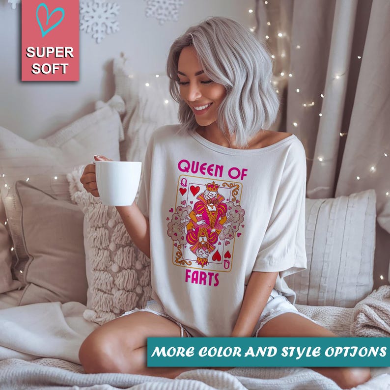 Op de afbeelding: Off-white t-shirt met een speelkaartafbeelding met de tekst "Queen of Farts". De afbeelding toont een cartoonkoningin en -koning met harten en kronen. Het shirt heeft ook de tekst "Super Soft" en "More Color and Style Options".