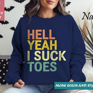 Puede incluir: Sudadera azul marino con la frase "HELL YEAH I SUCK TOES" en naranja, amarillo y verde. La sudadera es de cuello redondo. Las palabras "SUPER SOFT" est&aacute;n en un cuadrado rosa en la esquina superior izquierda.