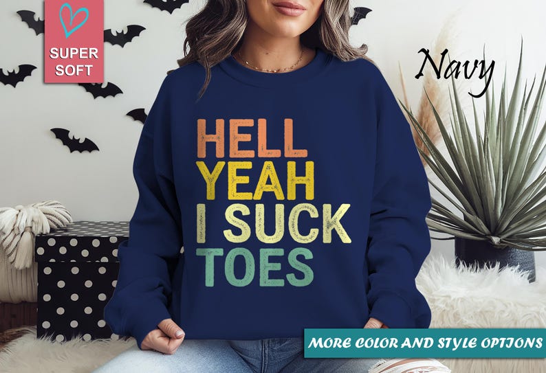 Puede incluir: Sudadera azul marino con la frase "HELL YEAH I SUCK TOES" en naranja, amarillo y verde. La sudadera es de cuello redondo. Las palabras "SUPER SOFT" est&aacute;n en un cuadrado rosa en la esquina superior izquierda.