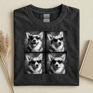 May include: Dark gray t-shirt featuring a square graphic of four black and white images of a Corgi dog wearing sunglasses. The shirt is made of a soft, comfortable material.