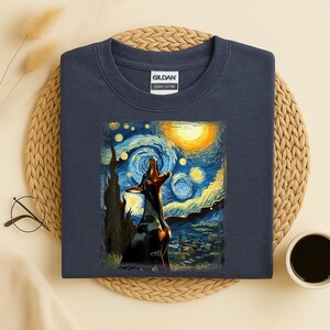 Puede incluir: Sudadera azul marino con un dise&ntilde;o de un perro aullando al estilo de "La noche estrellada" de Van Gogh. La obra de arte muestra un perro negro sobre un fondo de cielo nocturno azul oscuro y amarillo. La sudadera es de algod&oacute;n grueso.