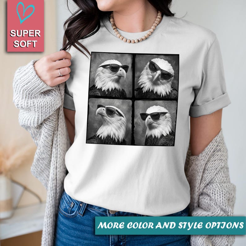 May include: White t-shirt featuring a black and white image of an eagle wearing sunglasses in four different poses. The shirt has the words "SUPER SOFT" and "MORE COLOR AND STYLE OPTIONS" printed on it.
