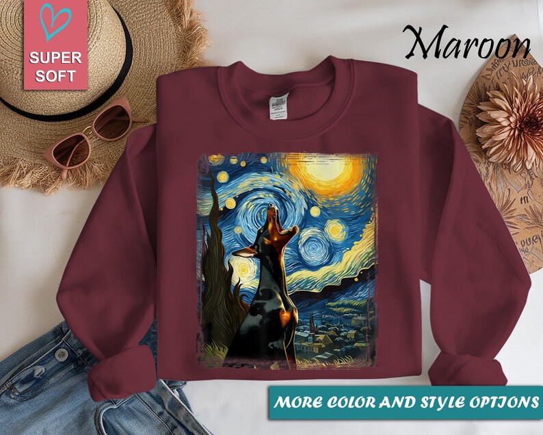 Puede incluir: Sudadera granate con un perro aullando a la luna, inspirada en "La noche estrellada" de Van Gogh. El dise&ntilde;o incluye una luna amarilla, un cielo arremolinado azul y amarillo, y un pueblo. El texto "Super Soft" est&aacute; en la parte superior izquierda.