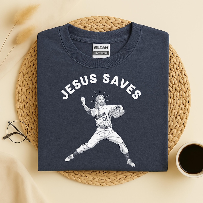 May include: Navy blue sweatshirt with the words "JESUS SAVES" in white block letters. A graphic of Jesus in a baseball uniform pitching a ball is below the text. The sweatshirt is made of heavy cotton.