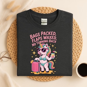 Puede incluir: Camiseta gris oscuro con el texto "BAGS PACKED, FLAPS WAXED, NO TURNING BACK." La camiseta presenta un unicornio de dibujos animados con gafas de sol y bikini, sosteniendo una maleta y una bebida tropical. El unicornio tiene melena y cola de arcoíris.