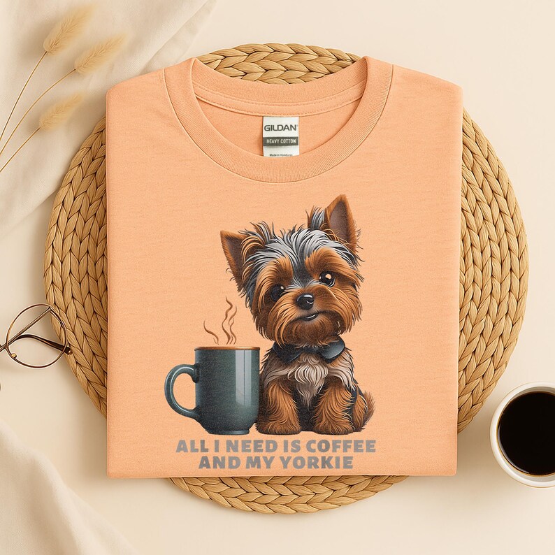 May include: Peach-colored t-shirt featuring a Yorkshire Terrier illustration with a coffee mug. The text "ALL I NEED IS COFFEE AND MY YORKIE" is printed below the image. The shirt is made of heavy cotton.
