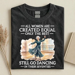 May include: Dark grey t-shirt featuring the text "ALL WOMEN ARE CREATED EQUAL - ONLY THE BEST - STILL GO DANCING - IN THEIR SEVENTIES." The graphic is a watercolour of a dancing woman.