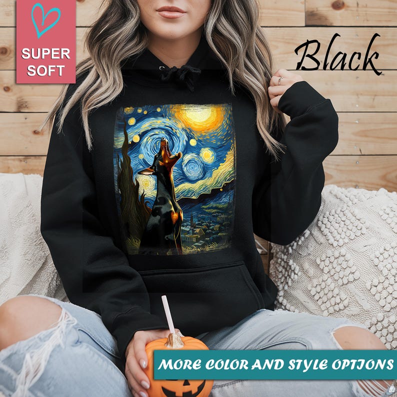 Puede incluir: Sudadera negra con un perro aullando a la luna, inspirada en "La noche estrellada" de Van Gogh. La sudadera tiene un bolsillo delantero y una capucha con cord&oacute;n. Las palabras "Super Soft" y "Black" est&aacute;n impresas en la sudadera. El texto "More color and style options" tambi&eacute;n es visible.