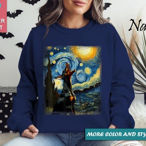 Puede incluir: Sudadera azul marino con un perro aullando a la luna, inspirada en "La noche estrellada" de Van Gogh. La obra de arte est&aacute; enmarcada. Las palabras "Super Soft" est&aacute;n en un cuadrado rosa. Las palabras "More color and style options" est&aacute;n en un rect&aacute;ngulo verde.