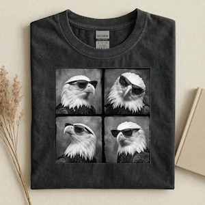 May include: Dark gray t-shirt featuring a square graphic of four black and white images of an eagle wearing sunglasses. The shirt is made of a soft, heavy cotton material.