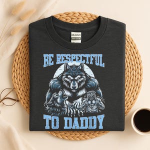 May include: Dark grey t-shirt with a wolf graphic and the text "BE RESPECTFUL TO DADDY" in light blue. The graphic features a central wolf with two smaller wolves on either side.