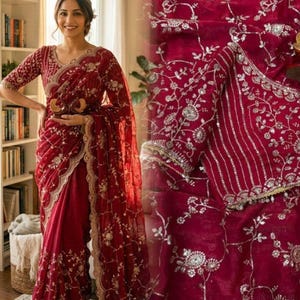 May include: A deep red saree with intricate silver embroidery and a matching blouse. The saree features floral and leaf patterns along the borders and across the fabric. The blouse has detailed embroidery on the sleeves and neckline, creating an elegant look.