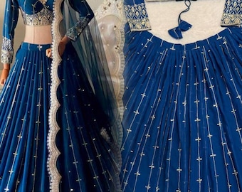 Può includere: Un vivace completo lehenga choli blu. L'ensemble presenta un top a maniche lunghe con intricati ricami dorati e una gonna plissettata abbinata. Un dupatta blu scuro trasparente con bordo smerlato e finiture dorate completa il look. L'outfit è esposto su un manichino.