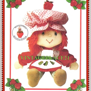 May include: A Strawberry Shortcake doll with red yarn hair, a pink and white polka-dot bonnet, and a red dress. The doll has a smiling face and is surrounded by strawberry illustrations. The text "STRAWBERRY" and "SHORTCAKE" are at the top and bottom.