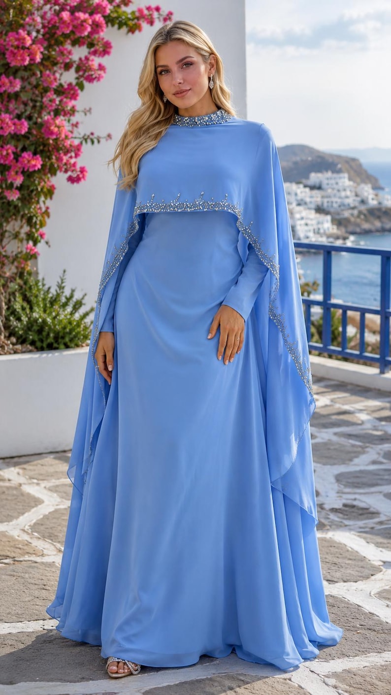 May include: A floor-length light blue gown featuring a high neckline and a cape-style overlay. The collar and the scalloped edge of the cape are embellished with silver beads and crystals. The dress has long sleeves and a flowing, full-length skirt.