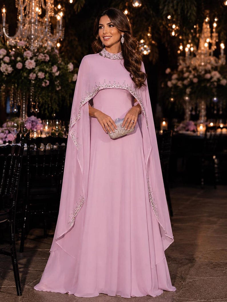 May include: A floor-length lavender gown featuring a high neckline and an attached cape overlay. The collar and the curved hem of the cape are embellished with silver beadwork and sequins. The dress is paired with a small, rectangular silver clutch.