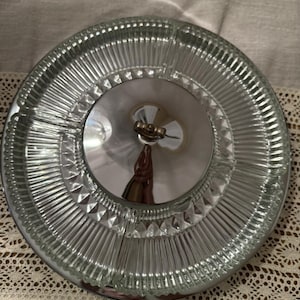 Könnte beinhalten: Eine Servierschale aus klarem Glas mit einem Deckel aus silberfarbenem Metall. Die Schale hat ein geripptes Design am Rand und ein Rautenmuster. Der Deckel hat einen kleinen Griff. Die Schale ist kreisförmig.