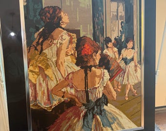May include: Needlepoint artwork depicting a group of women in ornate dresses, framed in black with a silver inner border. The scene appears to be a gathering or performance, with figures in various poses and colors.