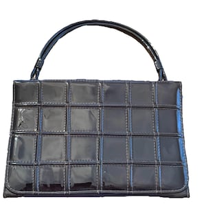 Puede incluir: Un bolso negro brillante con un patrón de cuadrícula y un asa curva. El bolso tiene forma rectangular con un acabado brillante y un diseño cosido. El asa también es negra y tiene un aspecto brillante.