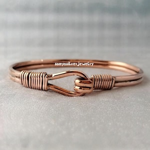 Könnte beinhalten: Ein roségoldenes Armband mit Haken- und Ösenverschluss. Das Armband hat ein gewickeltes Drahtdesign auf jeder Seite des Verschlusses. Der Text "somyasilver jewelry" ist auf dem Armband sichtbar.