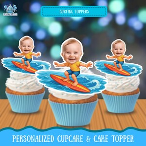May include: Three cupcakes in light blue liners topped with personalized paper cutouts featuring a smiling baby with a large head wearing a yellow shirt and blue shorts, surfing on a red surfboard over blue ocean waves with white foam.