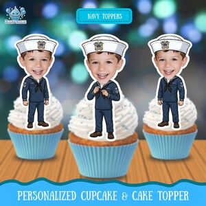 May include: Three cupcake toppers featuring a cartoon illustration of a smiling child wearing a navy blue sailor uniform and a white sailor hat with an emblem. The toppers are displayed on three cupcakes with white frosting in light blue liners.