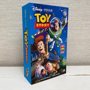 Puede incluir: Una caja azul de Toy Story con Woody, Buzz Lightyear y otros personajes. La caja tiene el logotipo de Disney Pixar y las palabras "Toy Story" en letras amarillas grandes. La caja también dice "Limited Release".