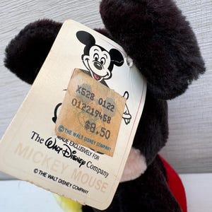 Puede incluir: Un peluche vintage de Mickey Mouse con una etiqueta. La etiqueta presenta el logotipo de Mickey Mouse, el texto "MADE EXCLUSIVELY FOR THE WALT DISNEY COMPANY MICKEY MOUSE" y una etiqueta de precio.