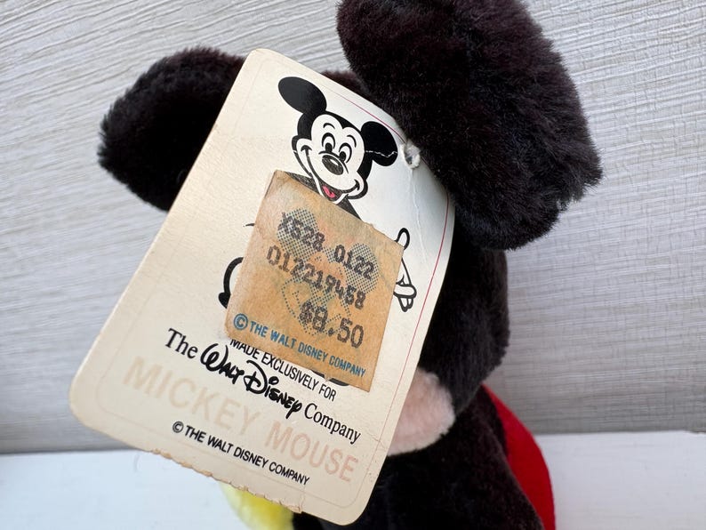 Puede incluir: Un peluche vintage de Mickey Mouse con una etiqueta. La etiqueta presenta el logotipo de Mickey Mouse, el texto "MADE EXCLUSIVELY FOR THE WALT DISNEY COMPANY MICKEY MOUSE" y una etiqueta de precio.