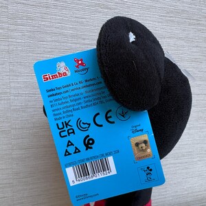 May include: A black plush Mickey Mouse toy with a blue tag. The tag features the Simba and Nicotoy logos, along with text and a barcode. The toy is a Disney product.