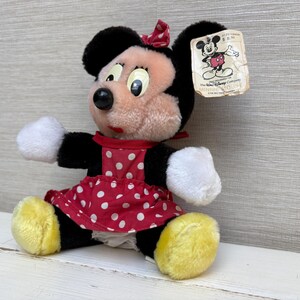 K&ouml;nnte beinhalten: Ein Vintage-Minnie-Mouse-Pl&uuml;schtier. Das Pl&uuml;schtier hat ein rot-wei&szlig; gepunktetes Kleid, schwarze Ohren und eine rote Schleife. Das Spielzeug hat ein Etikett mit einer Disney-Charakterillustration.