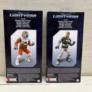 May include: Two action figure boxes featuring Buzz Lightyear from Disney Pixar's Lightyear. One box shows Buzz in an orange and white spacesuit, the other in a gray and white suit. The boxes have the Lightyear logo and text in multiple languages.