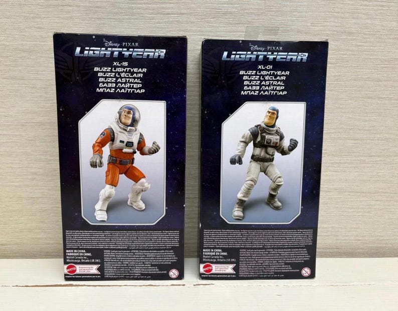 May include: Two action figure boxes featuring Buzz Lightyear from Disney Pixar's Lightyear. One box shows Buzz in an orange and white spacesuit, the other in a gray and white suit. The boxes have the Lightyear logo and text in multiple languages.