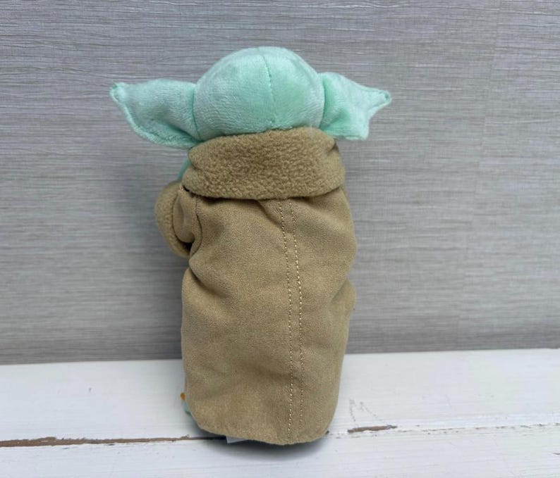 May include: A plush toy of a character with large ears and a tan coat. The toy has a light green head and ears, with a tan coat and a brown collar. The toy is made of soft fabric and is designed to resemble a popular character.