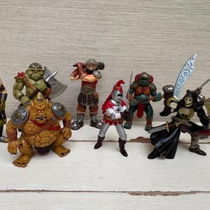 May include: A collection of fantasy action figures, including warriors, skeletons, and mythical creatures. The figures are in various poses, some holding weapons like swords and axes. The color palette includes shades of green, brown, red, and silver.