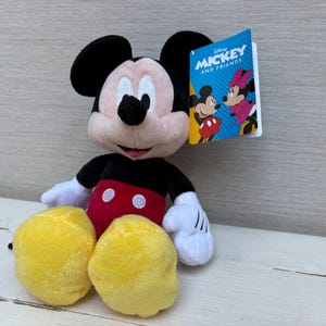 May include: A plush Mickey Mouse doll with black ears, a black body, red shorts, and yellow feet. The doll has white gloves and a tag that reads "Mickey and Friends."