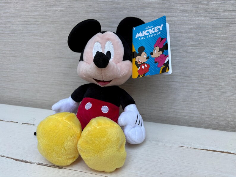 May include: A plush Mickey Mouse doll with black ears, a black body, red shorts, and yellow feet. The doll has white gloves and a tag that reads "Mickey and Friends."