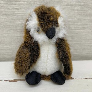May include: A plush owl toy with brown, white, and black accents. The owl has a fluffy brown and white head, a white chest, and black feet. The toy is made of soft, textured materials and is designed to resemble an owl.