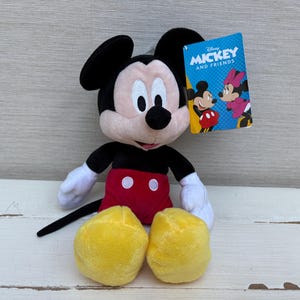 May include: A plush Mickey Mouse toy with black ears, a black body, white gloves, red shorts, and yellow shoes. A tag reads "Mickey and Friends" with images of Mickey and Minnie Mouse.