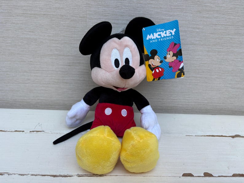 May include: A plush Mickey Mouse toy with black ears, a black body, white gloves, red shorts, and yellow shoes. A tag reads "Mickey and Friends" with images of Mickey and Minnie Mouse.