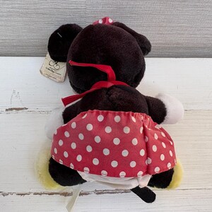 K&ouml;nnte beinhalten: Eine Pl&uuml;schpuppe von Minnie Mouse, von hinten gesehen, hat einen schwarzen Kopf und Ohren, eine rote Schleife und einen rot-wei&szlig; gepunkteten Rock. Die Puppe hat wei&szlig;e Handschuhe und gelbe Schuhe. Ein Etikett ist angebracht.