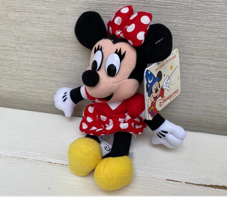 May include: A Minnie Mouse soft toy, dressed in a red and white polka dot dress and bow. The toy has black ears, a black nose, and white gloves. A Disneyland tag is attached.