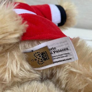 May include: Close-up of a plush toy with tan fur and a red hat with white trim. A tag with the text "Historic Royal Palaces" and a website address is visible.