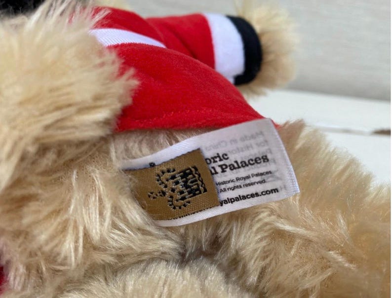 May include: Close-up of a plush toy with tan fur and a red hat with white trim. A tag with the text "Historic Royal Palaces" and a website address is visible.